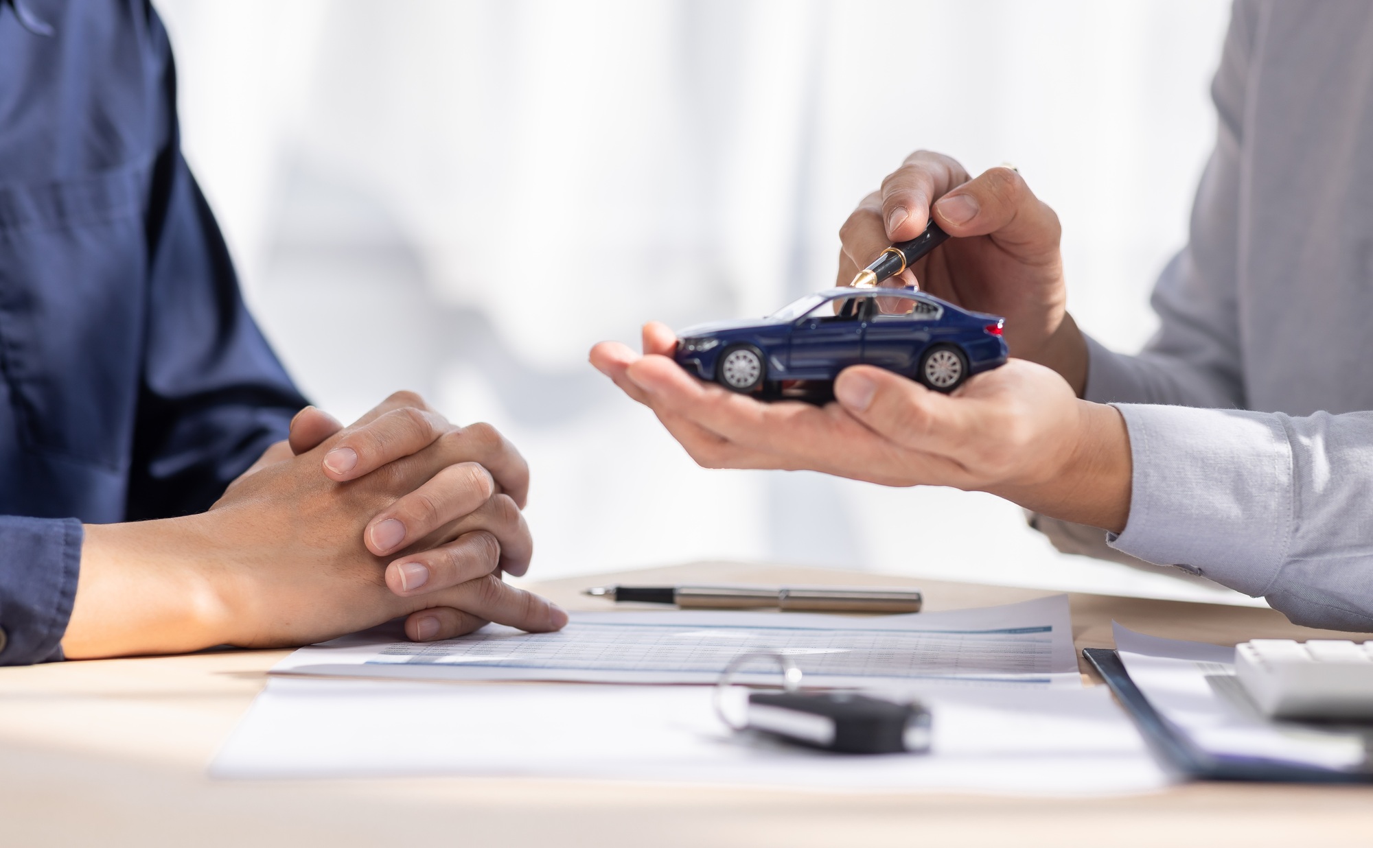 Dealer salesman giving car key to owner. client signing insurance document or rental car lease form